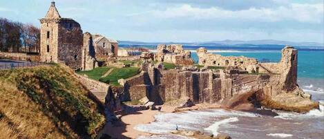 A historic stone castle with ruins, a tower, and a beach in the foreground.
