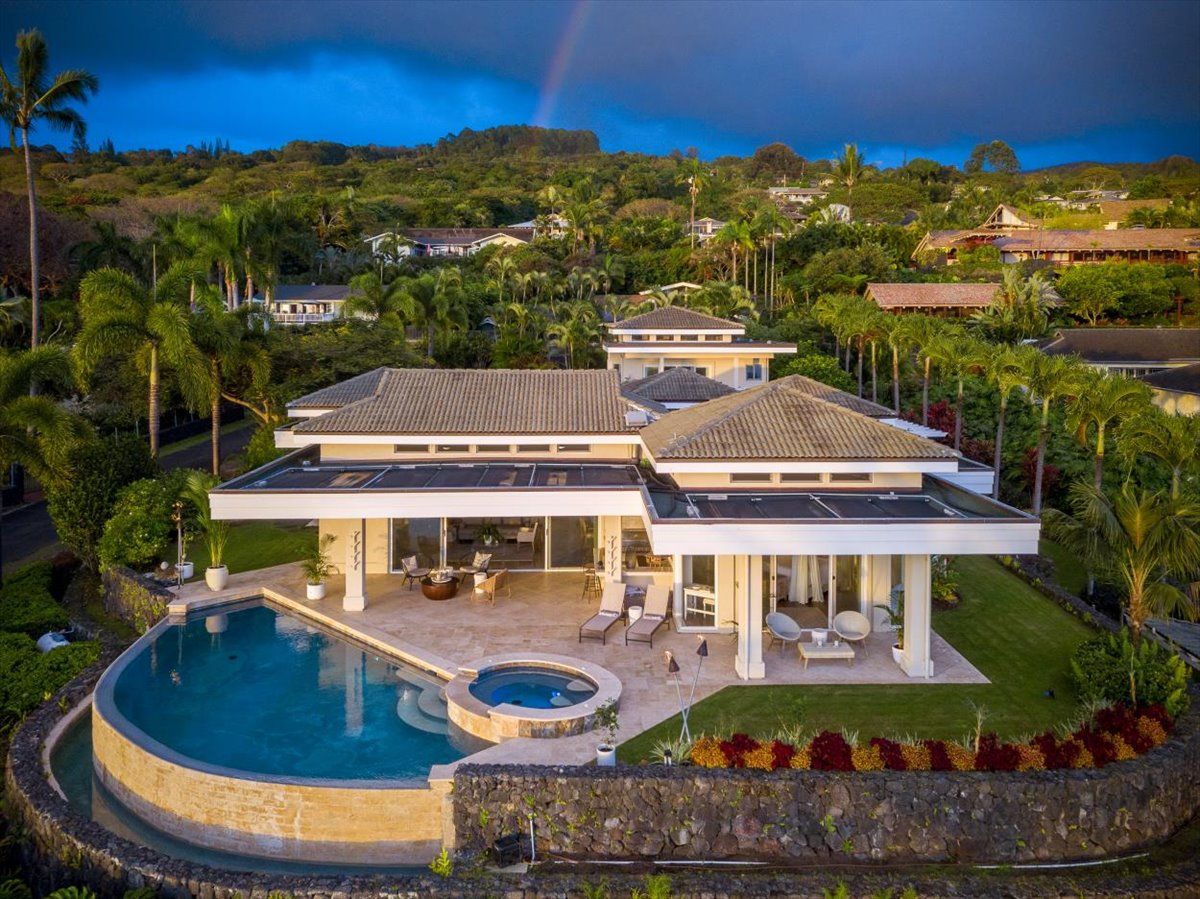A modern house with a large swimming pool, a covered patio, and lush landscaping.