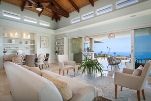 A spacious living area with a large sofa, chairs, a dining table, and a view of the ocean. - Puuwai Alii Estate: Stunning Luxury Home with Pool, Hot Tub & Ocean Views,AC! (Kailua Kona)