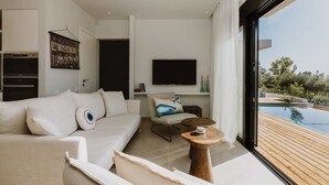 Un salon moderne avec un canapé blanc, un téléviseur à écran plat et une terrasse en bois donnant sur une piscine.
