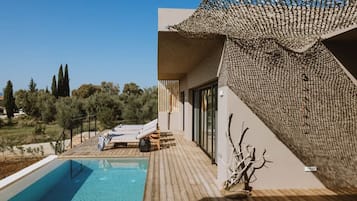 A modern outdoor pool area with a wooden deck, lounge chairs, and a view of the surrounding landscape.