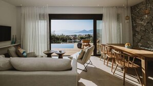 Un salon moderne comprenant un canapé, une table à manger et des chaises, un téléviseur, et offrant une vue sur une piscine et des montagnes.