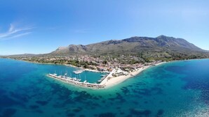 Vue aérienne d’une ville côtière avec un port de plaisance, des eaux d’un bleu limpide et une montagne en arrière-plan.