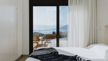 A bedroom with a large bed, a view of a balcony with outdoor furniture, and a sliding glass door leading to a scenic outdoor area.