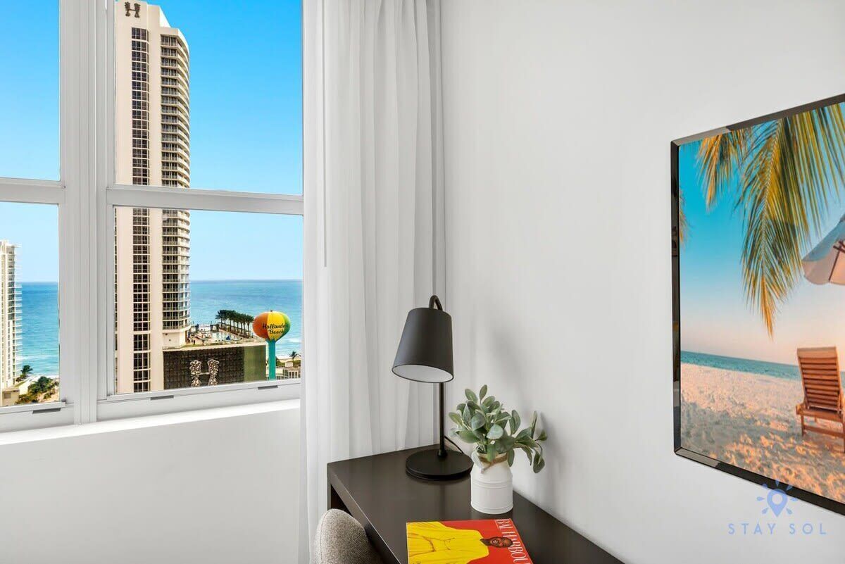 A hotel room with a large window offering a view of a tall building and the ocean.