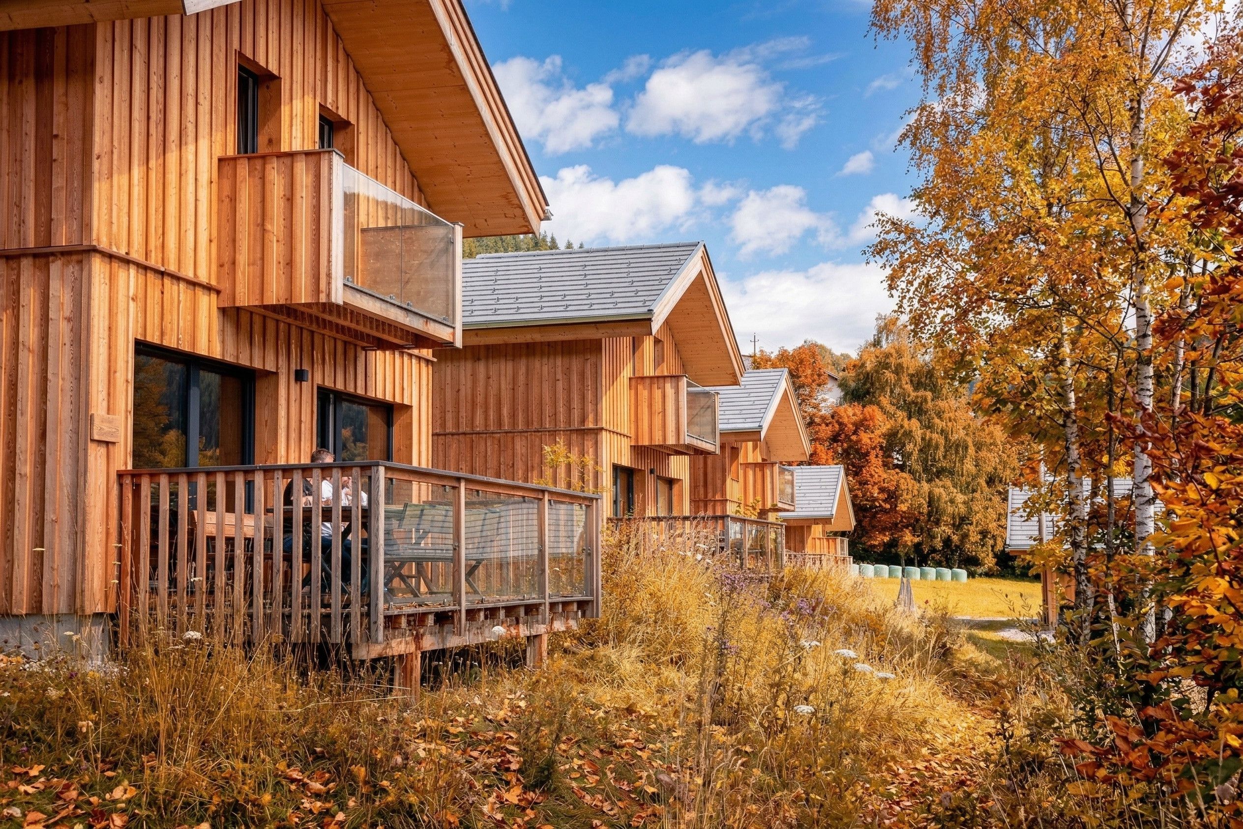 Een houten chalet met een balkon, omgeven door herfstkleuren.