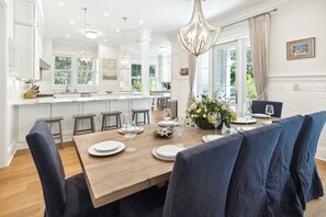 Une cuisine moderne avec des meubles blancs, un îlot central en bois et un coin repas doté de chaises recouvertes d’un tissu bleu.