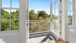 Ein Balkon mit weißen Geländern und Holzboden, der Blick auf grüne Bäume und einen klaren Himmel gewährt.