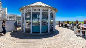 Ein Pavillon mit Glasveranda auf einer Holzterrasse, umgeben von Tischen und Stühlen.