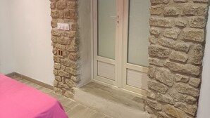 Une pièce avec un mur en pierre, une porte-fenêtre coulissante et un lit recouvert d’une couverture rose.