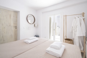 A modern hotel room with a large bed, a wooden wardrobe, a mirror, and a clothing rack with towels.