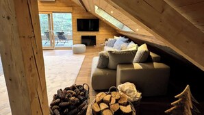 A cozy attic living room with a wooden ceiling, a large window, a flat-screen TV, a grey sofa, and a fireplace. - Splendid 4-star apartment facing the mountains (La Bresse)