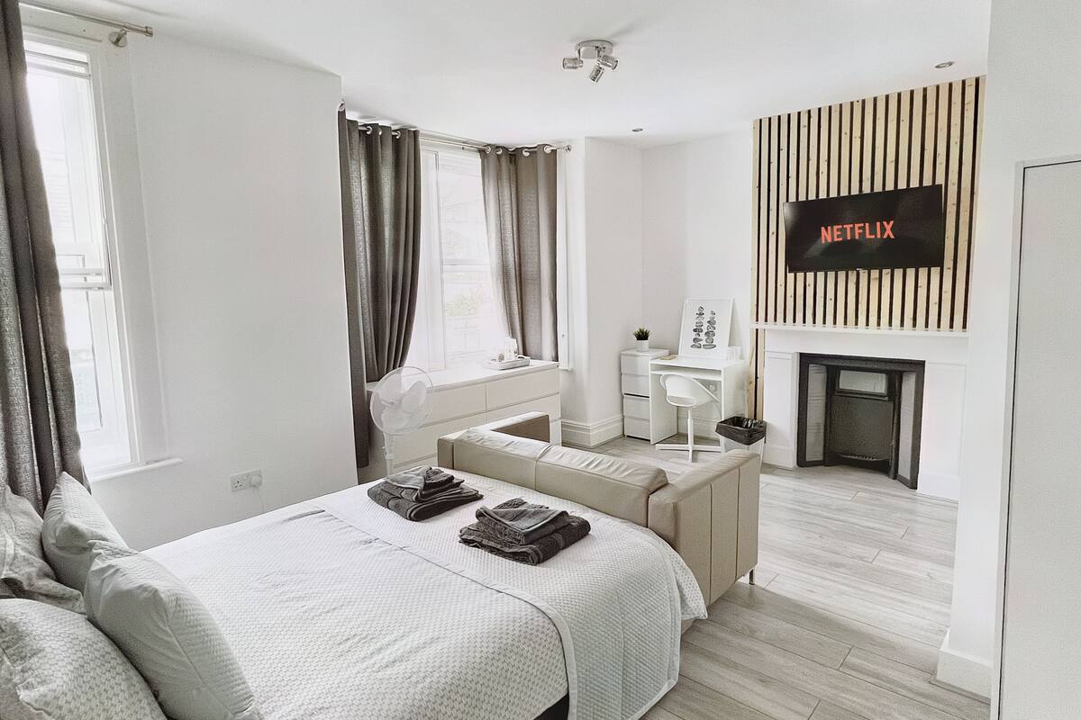 A modern bedroom with a bed, a sofa, a desk, and a fireplace.