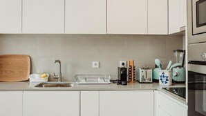 Une cuisine moderne avec des meubles blancs, un évier en acier inoxydable, une planche à découper en bois, une machine à café, un grille-pain et un mixeur.