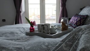 A neatly made bed with a tray of breakfast items including a teapot, cups, and a small vase with flowers. - Montesanto 77 Panoramic house in the historic center (Napoli)