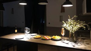 A dining area with a long table, two pendant lights, a vase with flowers, and a bottle of wine. - Montesanto 77 Panoramic house in the historic center (Napoli)