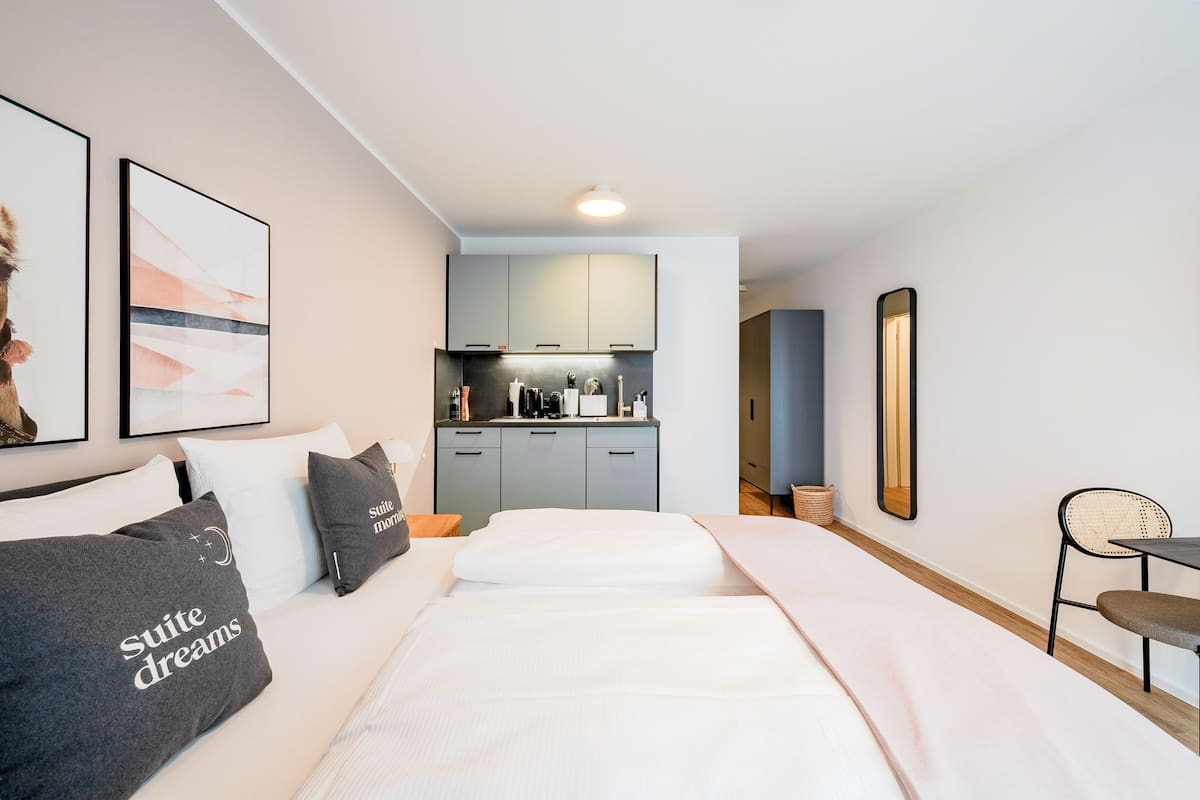 Una habitación de hotel con cama, escritorio, silla, kitchenette y baño.
