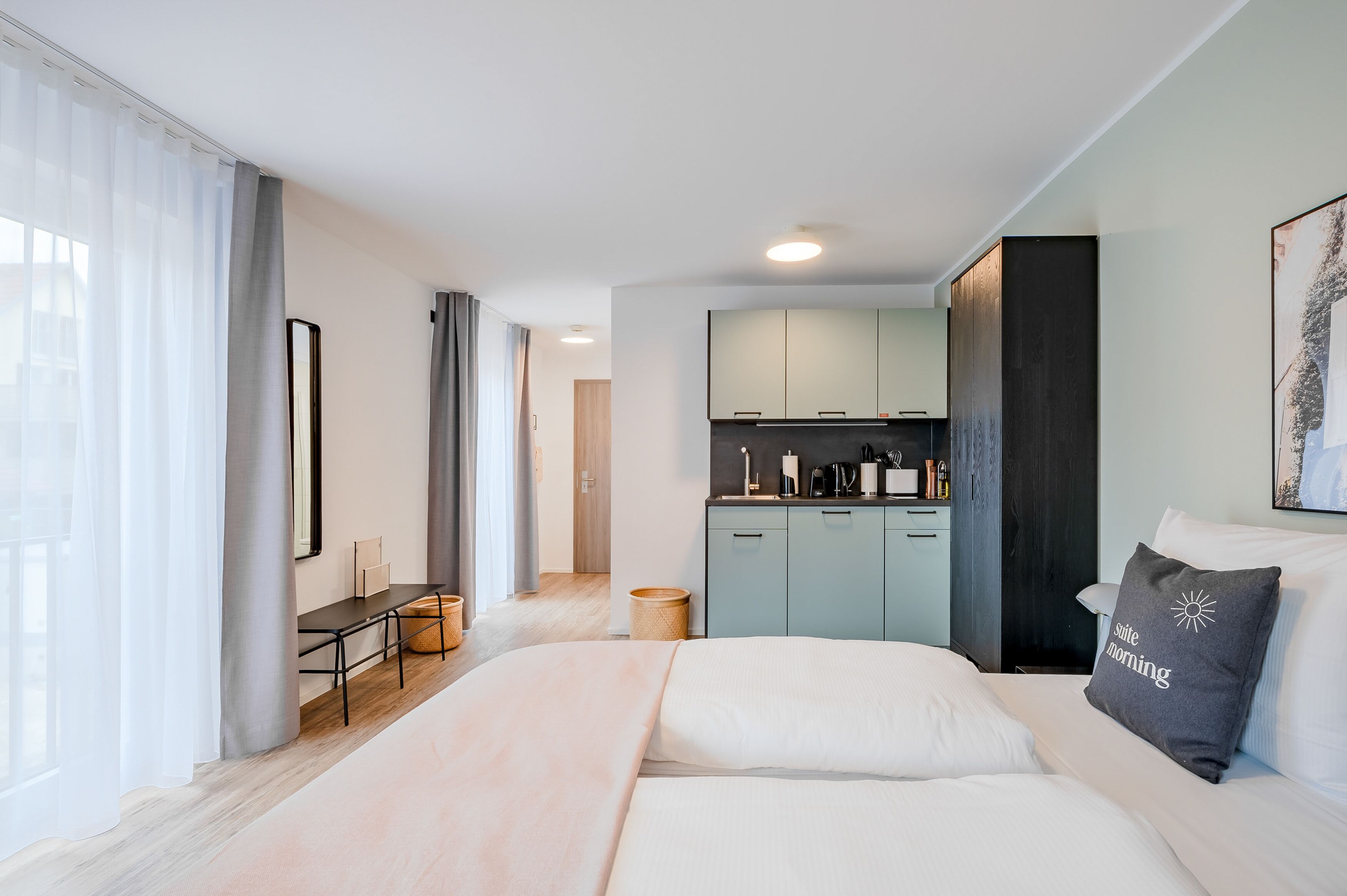 A modern hotel room with a bed, a desk, and a kitchenette.