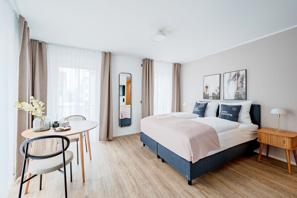 A modern hotel room with a bed, bedside table, lamp, and a dining area with a table and chairs. - Limehome Metzingen Wilhelmstr. (Metzingen)