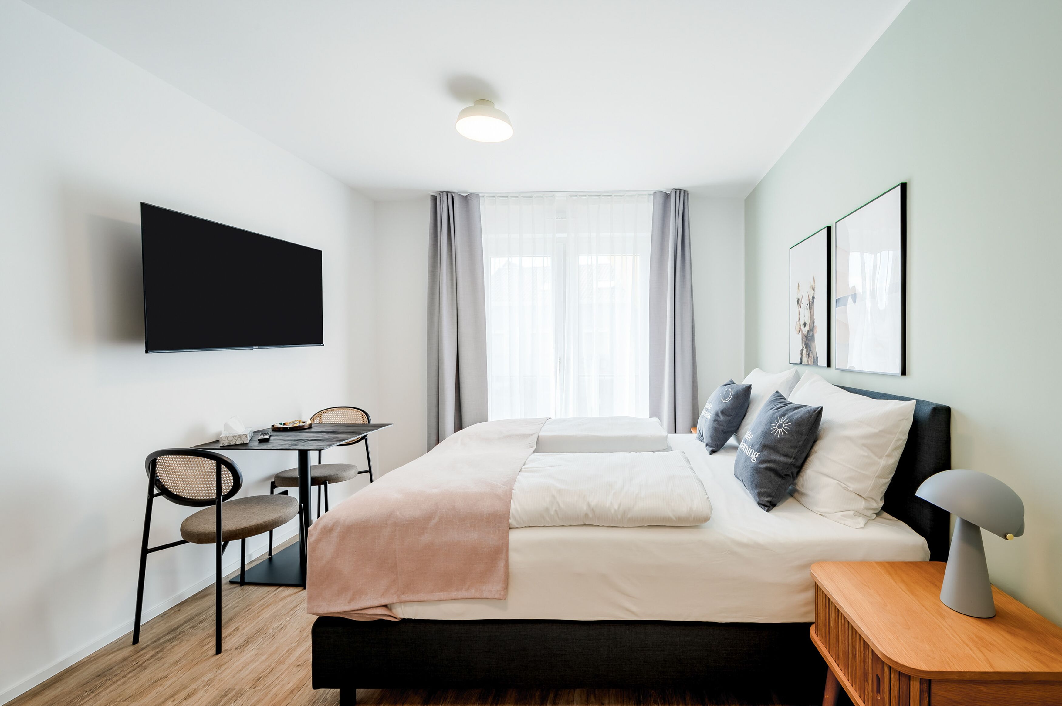 Et moderne hotelværelse med en seng, et natbord og et fjernsyn ophængt på væggen.