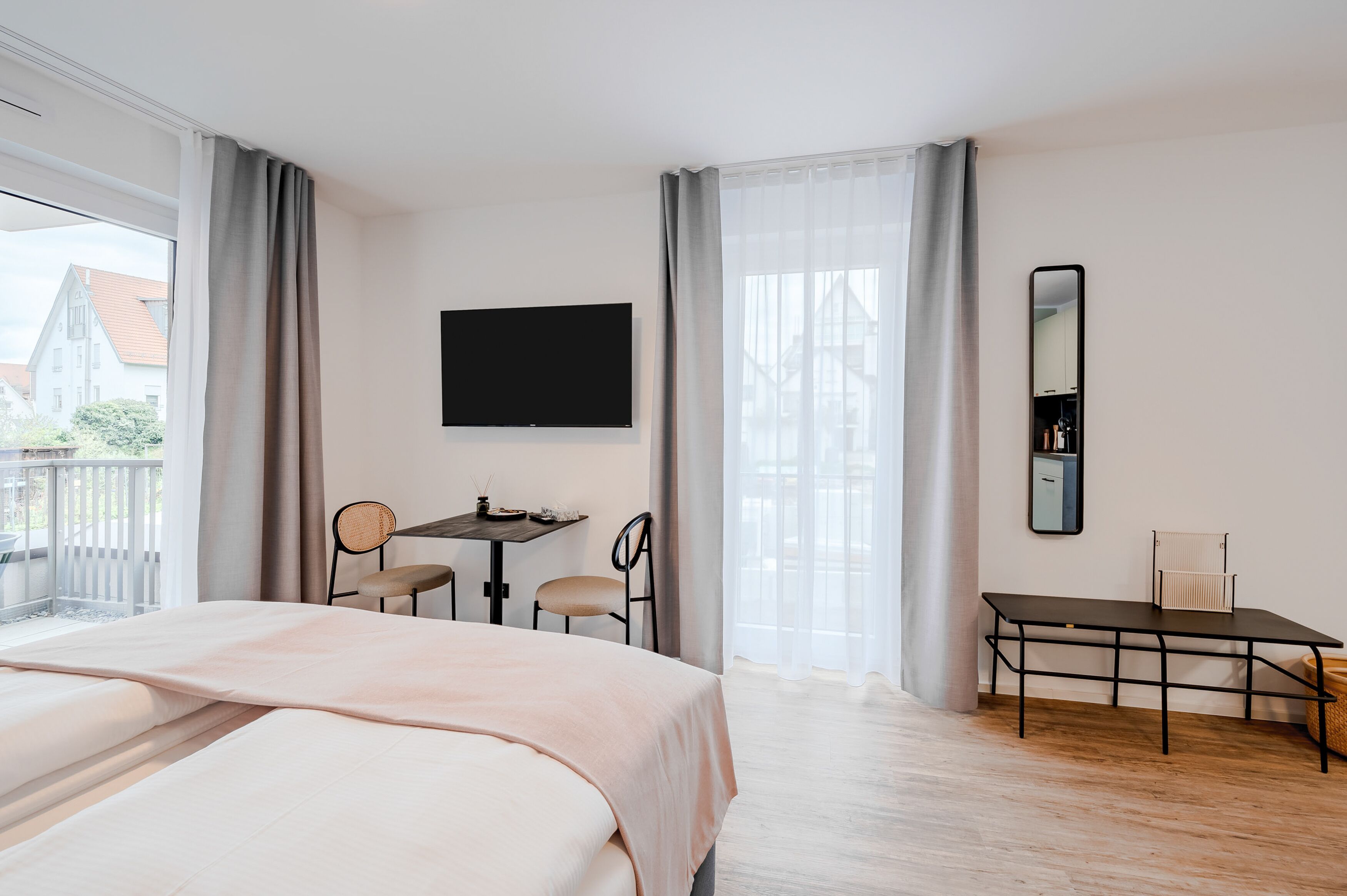 A hotel room with a bed, a desk with chairs, a TV, and a large window with curtains.