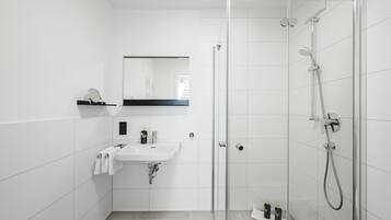 Une salle de bain moderne avec une douche à parois de verre, un lavabo blanc et un miroir au-dessus.