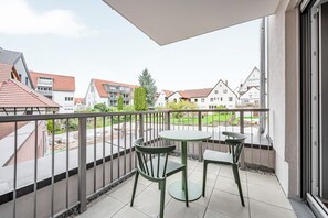 A balcony with a table and two chairs, overlooking a residential area with houses and greenery. - Limehome Metzingen Wilhelmstr. (Metzingen)