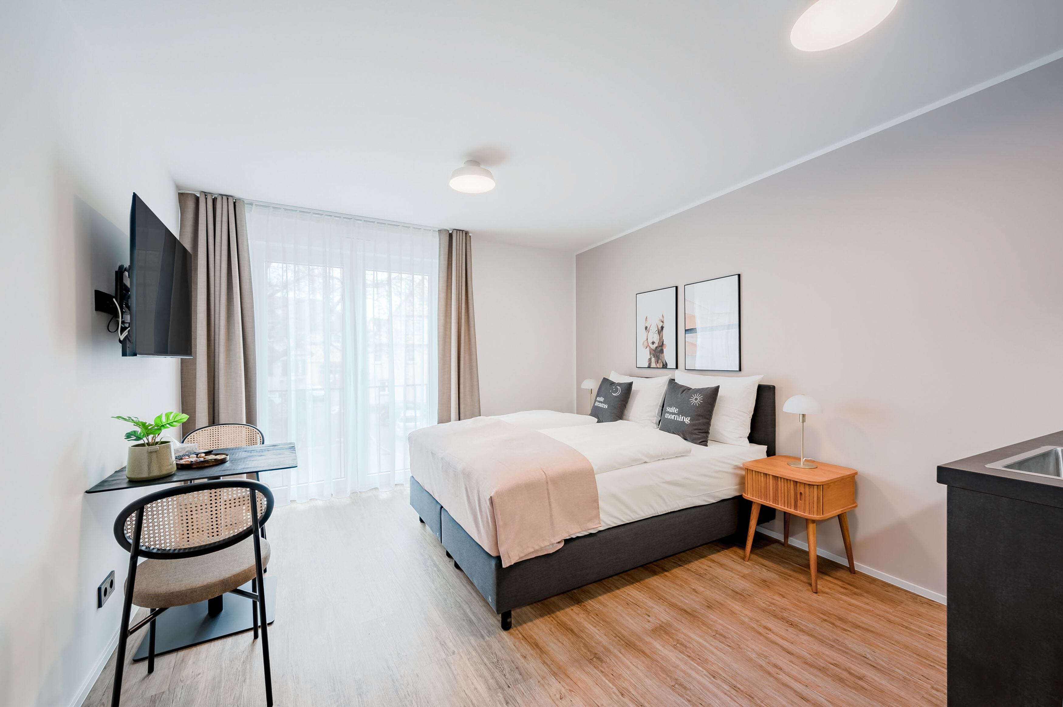A modern bedroom with a bed, bedside table, TV, and a desk with a chair.