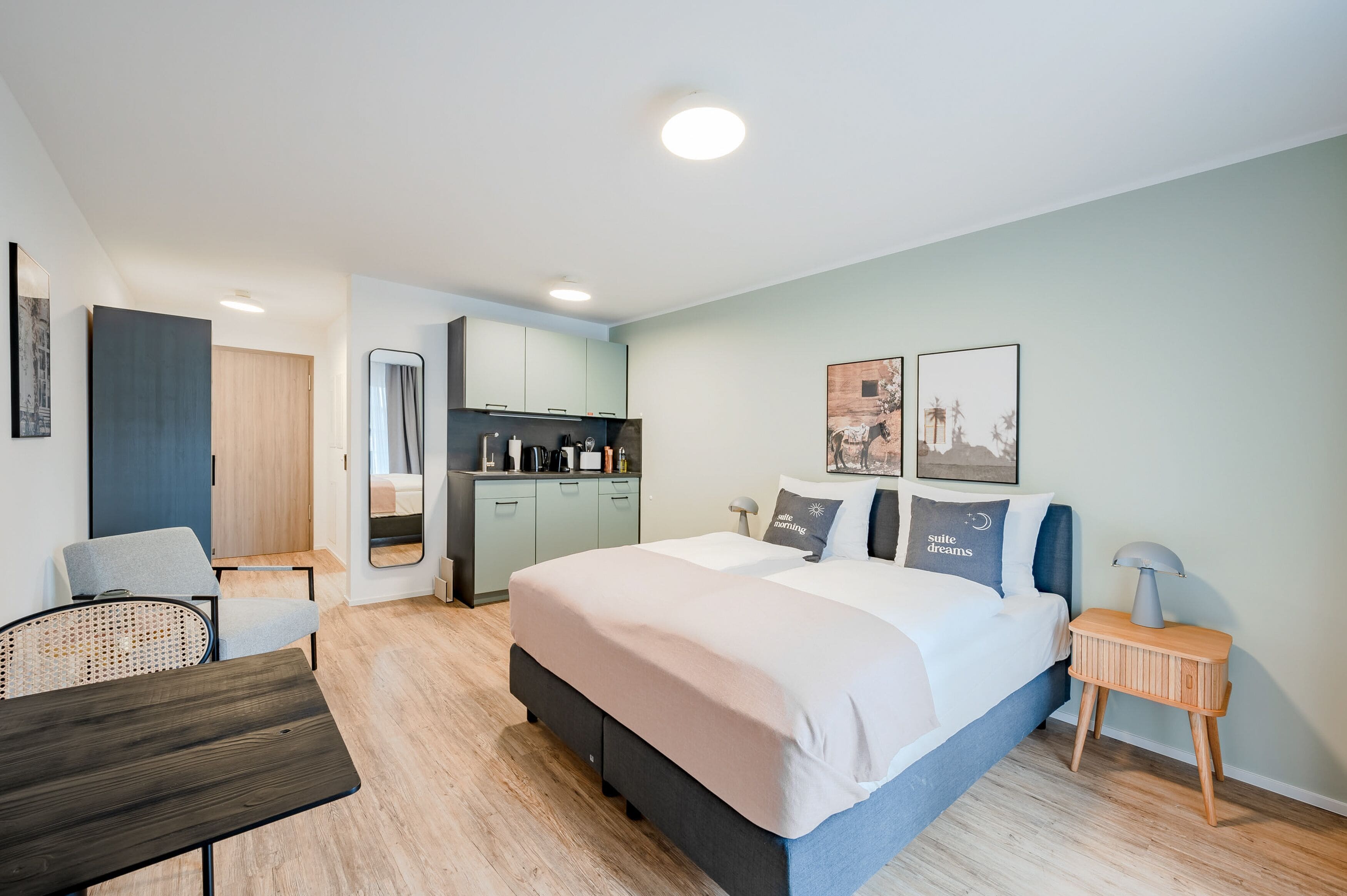 Une chambre d’hôtel moderne équipée d’un grand lit, d’un bureau, d’une chaise, d’une petite kitchenette et d’une salle de bain.