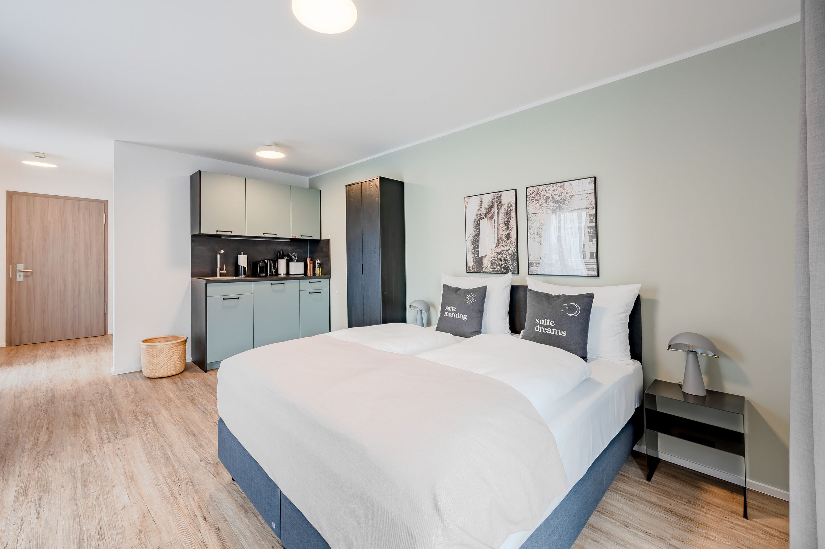 A modern hotel room with a large bed, a small kitchenette, and a view of the city.