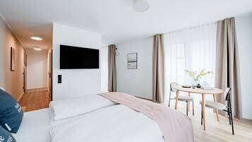 Une chambre d’hôtel avec un lit, un bureau et une chaise. Il y a un téléviseur fixé au mur et une fenêtre avec des rideaux.