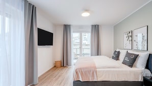 Un dormitorio moderno con una cama grande, cortinas grises, un televisor de pantalla plana y obras de arte en la pared.