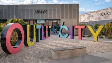 Ein modernes Gebäude mit den Hinweisschildern 'ARMANI' und 'GUCCI', umgeben von farbenfrohen, großen Buchstaben, die 'OUTLOOK' buchstabieren.