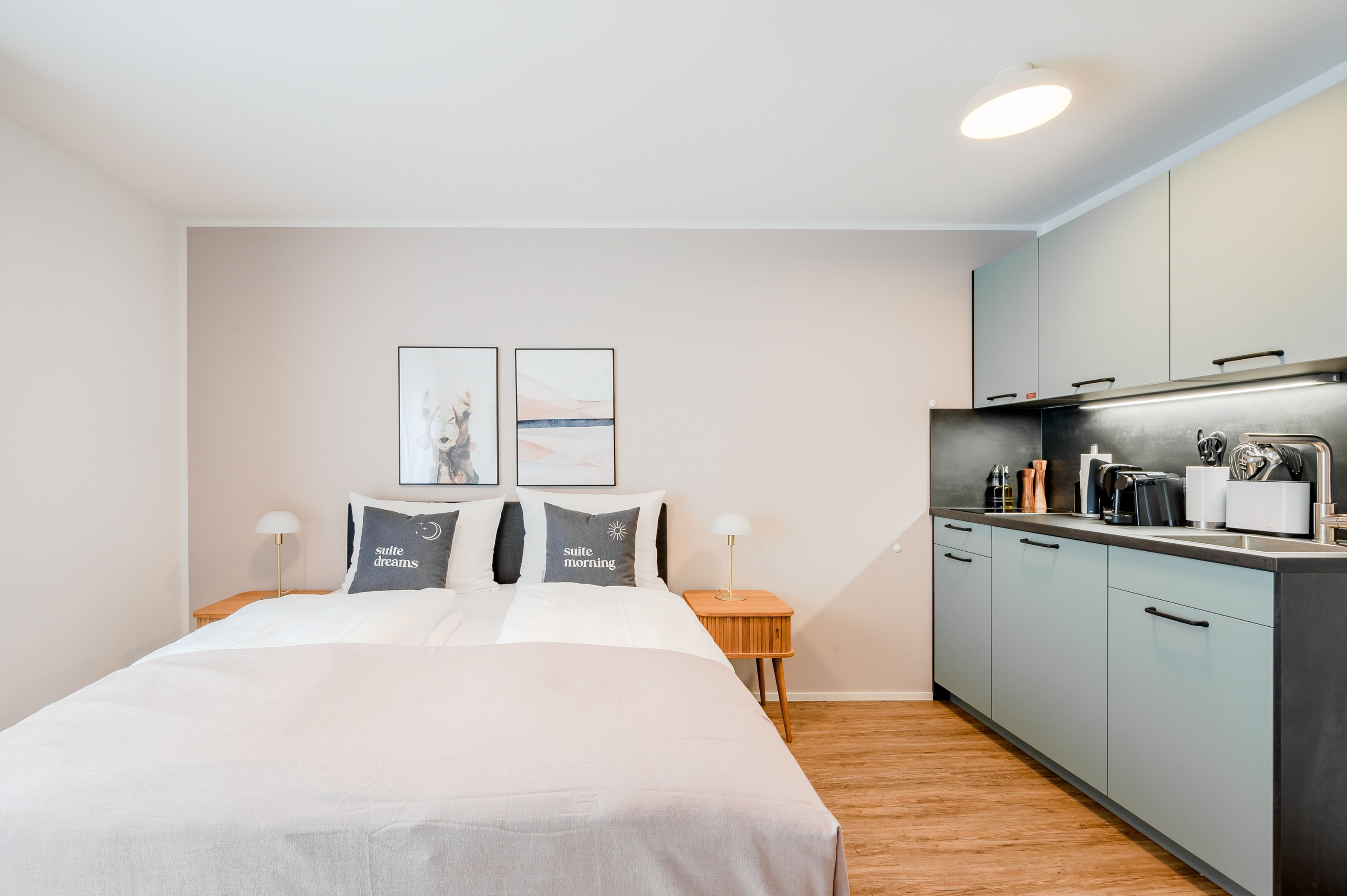 Een moderne hotelkamer met een groot bed, een klein kitchenette en twee ingelijste foto’s aan de muur.