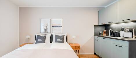 A modern hotel room with a large bed, a small kitchenette, and two framed pictures on the wall.