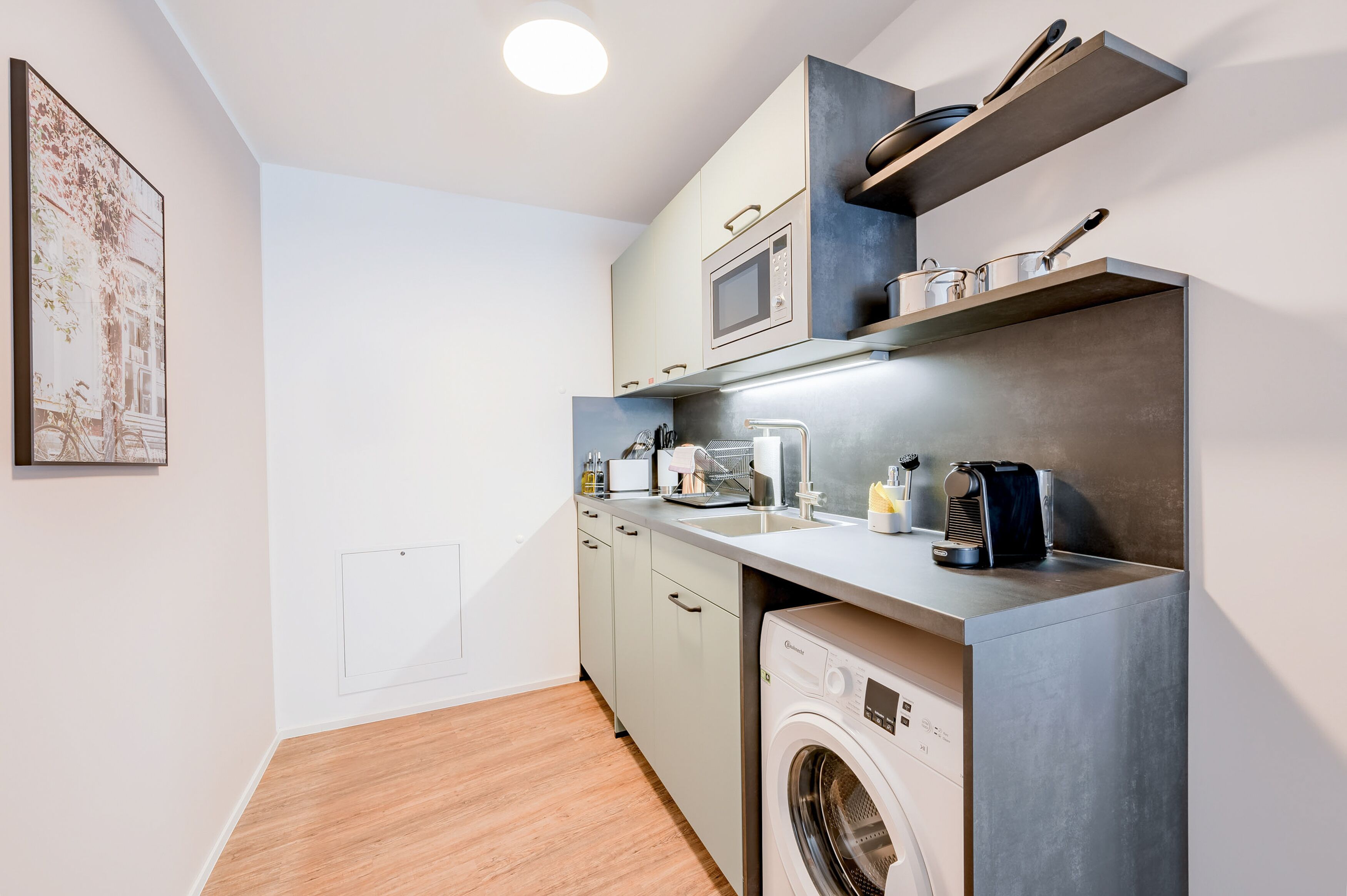 Une cuisine compacte équipée d’un lave-linge, d’un four à micro-ondes et de petits appareils électroménagers.