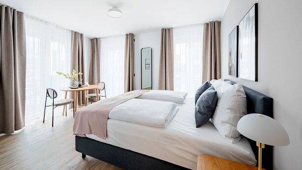 Una habitación de hotel moderna con una cama grande, una mesita de noche y un escritorio con una silla.