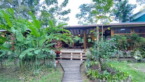A wooden pathway leading to a covered outdoor seating area surrounded by lush greenery and various plants. - White Beach Jungle Villa and Private Pool, National Park Cahuita (Cahuita)