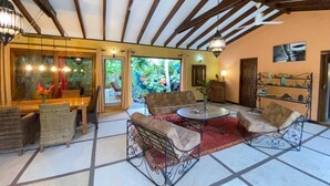 A spacious indoor area with a high ceiling, a dining table with chairs, a seating area with a round table, and a view of greenery outside. - White Beach Jungle Villa and Private Pool, National Park Cahuita (Cahuita)
