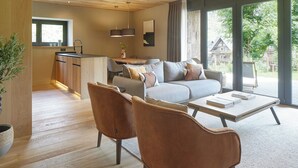 A modern living room with a sofa, two armchairs, a coffee table, and a view of the outdoors through large windows.
