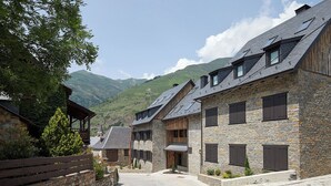 A row of stone buildings with sloped roofs and wooden shutters, set against a mountainous backdrop.
