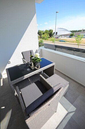A balcony with a wicker table and chairs, a potted plant, and a view of a stadium. - Luxury Majpruz Suites I (Zadar)