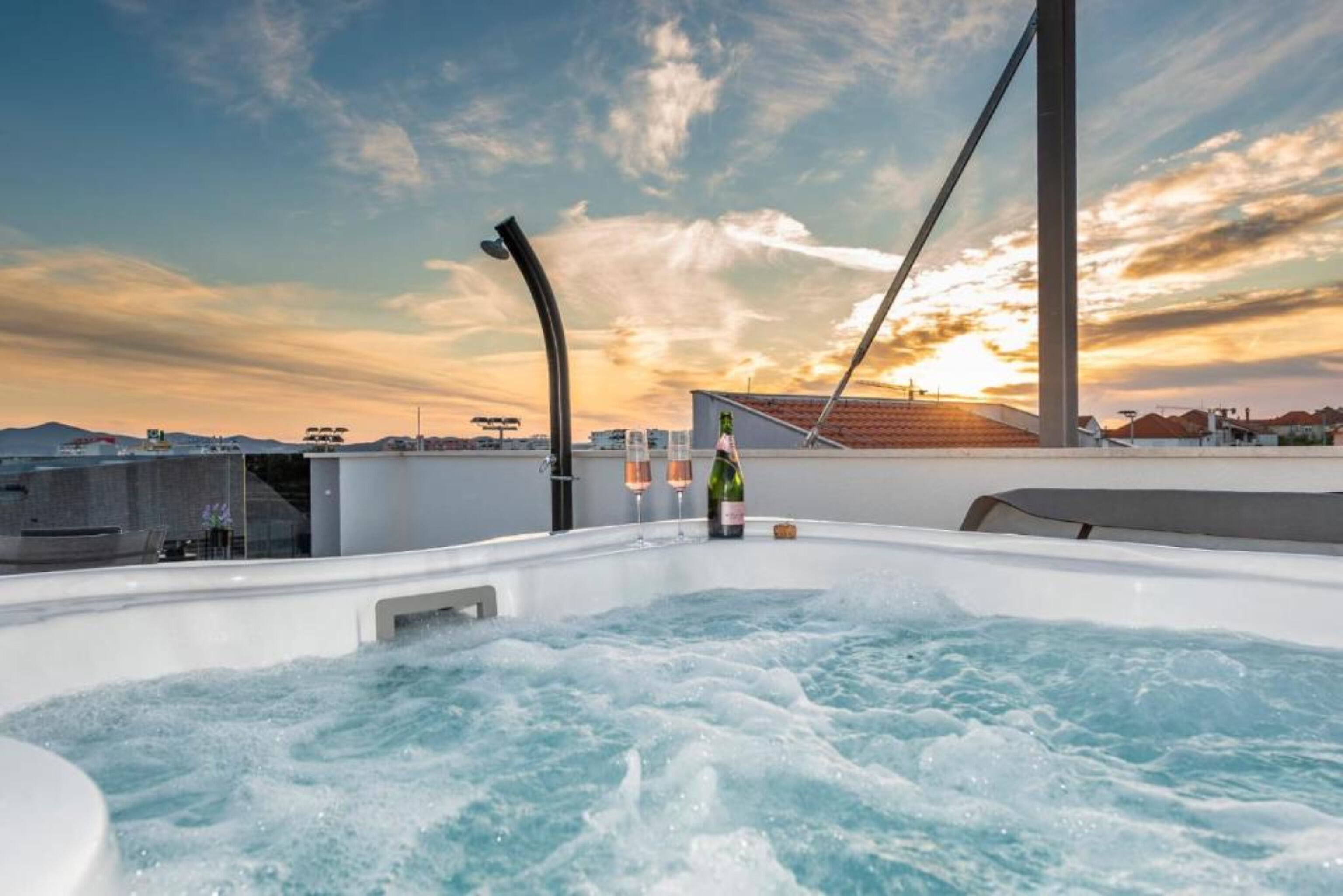 Un jacuzzi con vista al atardecer, una botella de champán y un puente moderno al fondo.