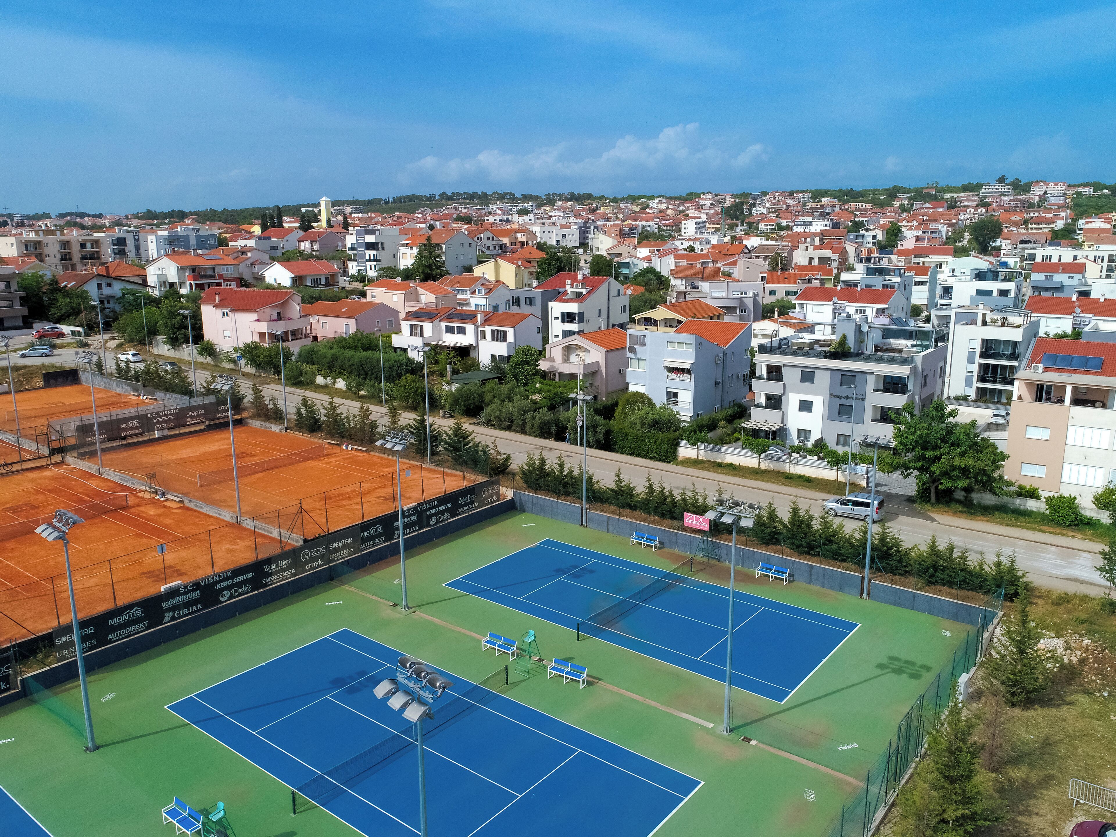 A tennis court complex with multiple courts, surrounded by residential buildings.