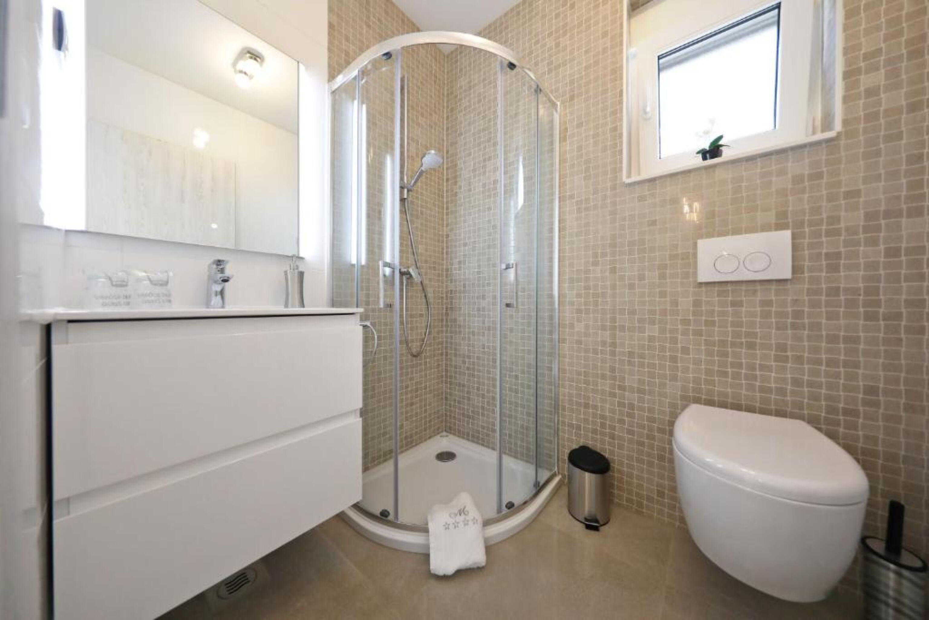 A modern bathroom with a glass-enclosed shower, a white toilet, and a sink with a mirror.