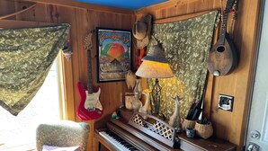 A cozy room with a wooden piano, a guitar, a lamp, and a framed poster on the wall. - Nature Retreat, Pet Friendly Cozy Cabin On 80 Acres With Fields & Forrest Trails (Fort Edward)