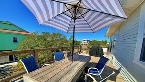 Een houten terras met een tafel, stoelen en een parasol, met uitzicht op een huis en bomen.