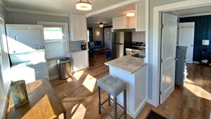 Een moderne keuken met een centraal eiland, inbouwapparatuur en een eethoek met een houten tafel en een barstoel.