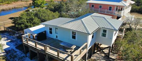 A coastal house with a deck and a covered area, surrounded by natural vegetation and a body of water.