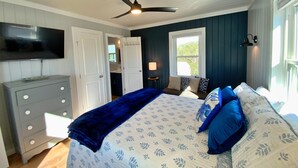 Een slaapkamer met een bed, een plafondventilator, een televisie, een dressoir en een raam.